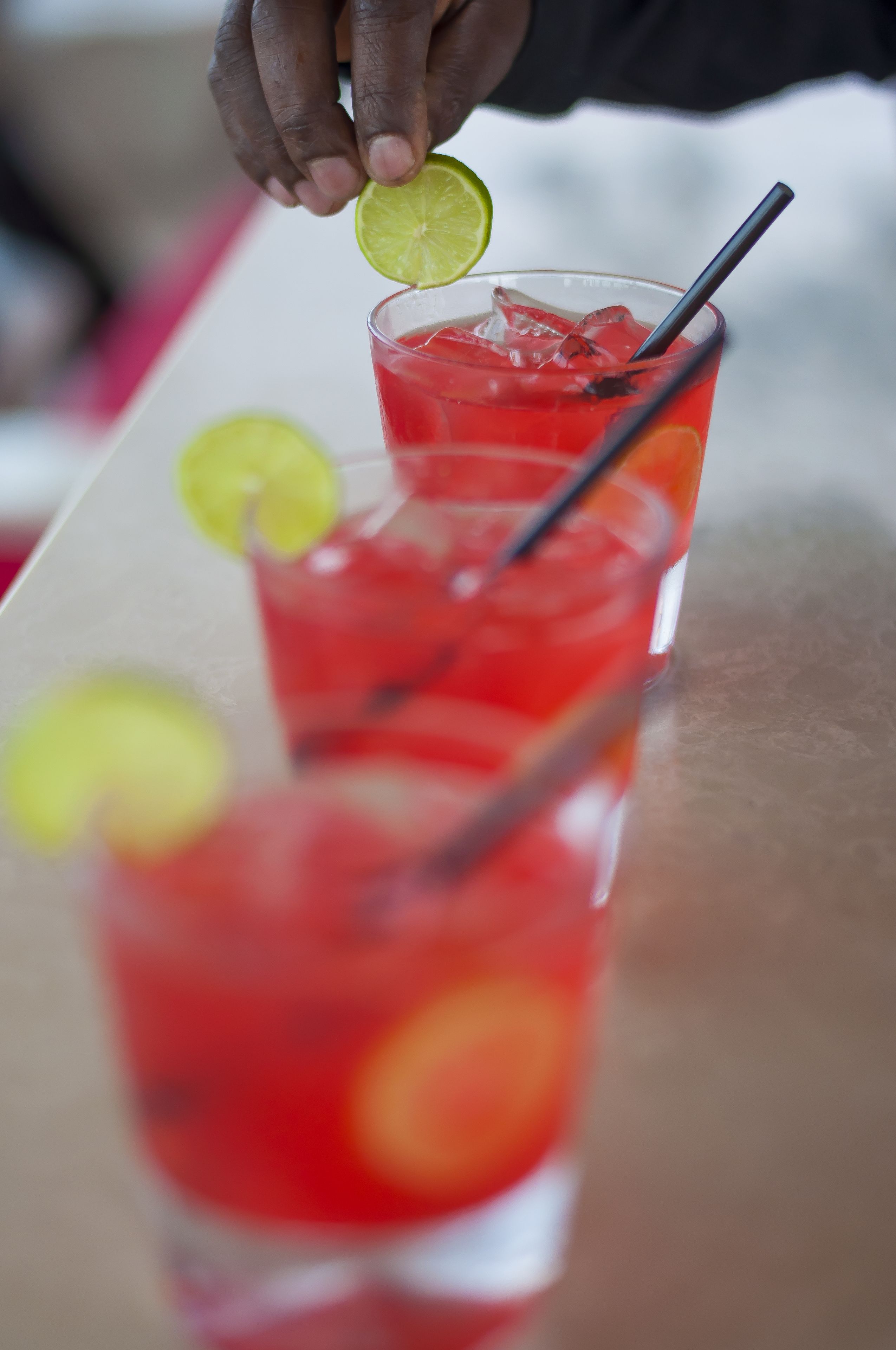 A row of red drinks with lime slices and straws on a table.