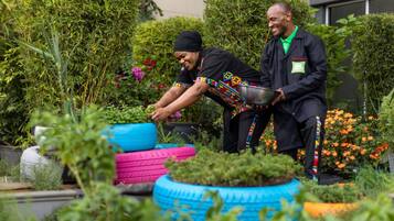 Dos personas trabajando en un jardín exuberante, con mucha vegetación y coloridos maceteros hechos con neumáticos.