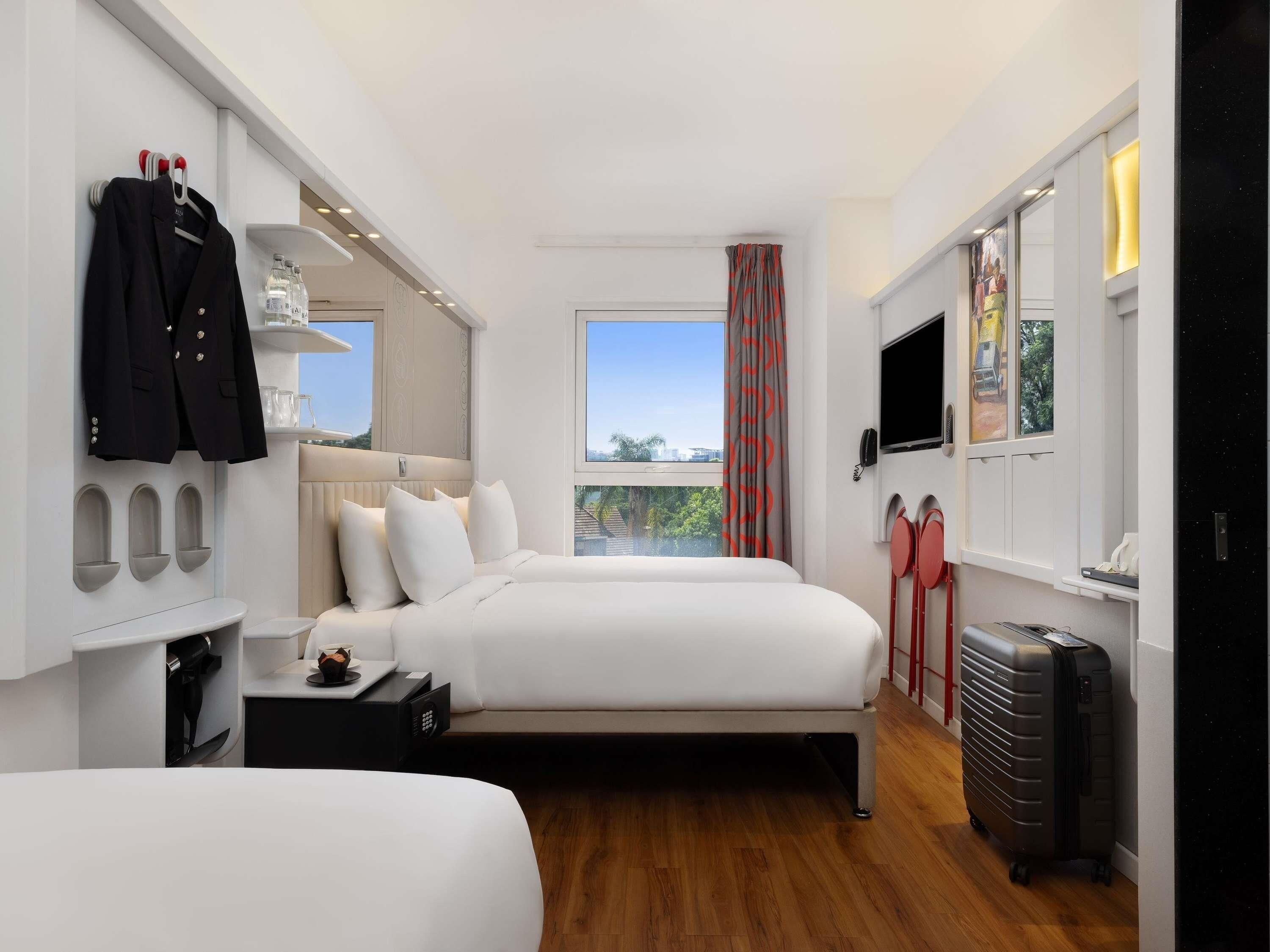 A modern hotel room with two beds, a TV, a desk, and a view of the outdoors.