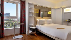 Habitación de hotel con una cama grande, mesitas de noche, una pequeña mesa redonda, un microondas y una ventana con cortinas.