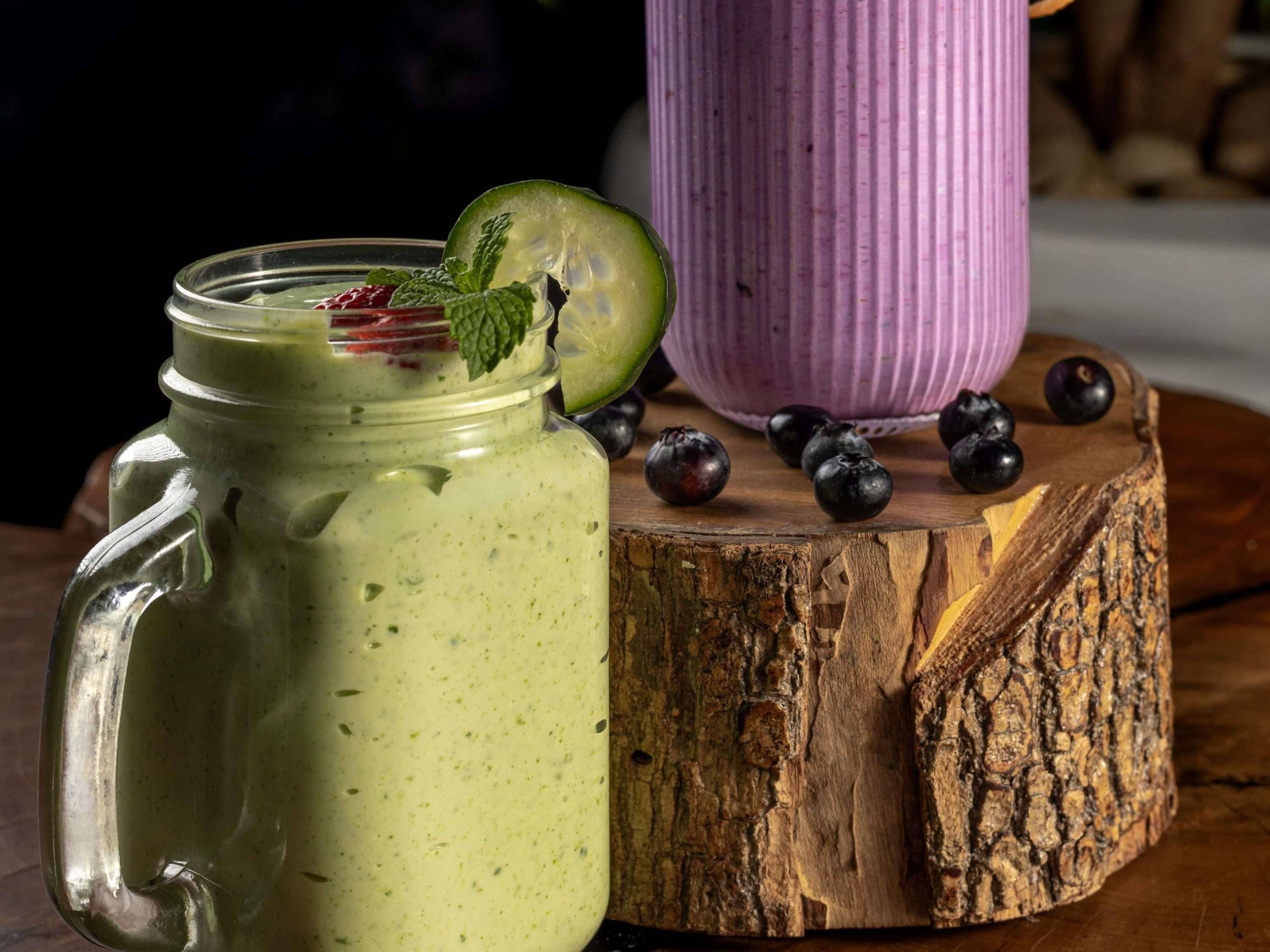 A mason jar with a green smoothie, a wooden cutting board, and a purple container.