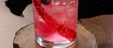 Un verre contenant une boisson rose, des glaçons et une garniture rouge, posé sur une surface en bois.