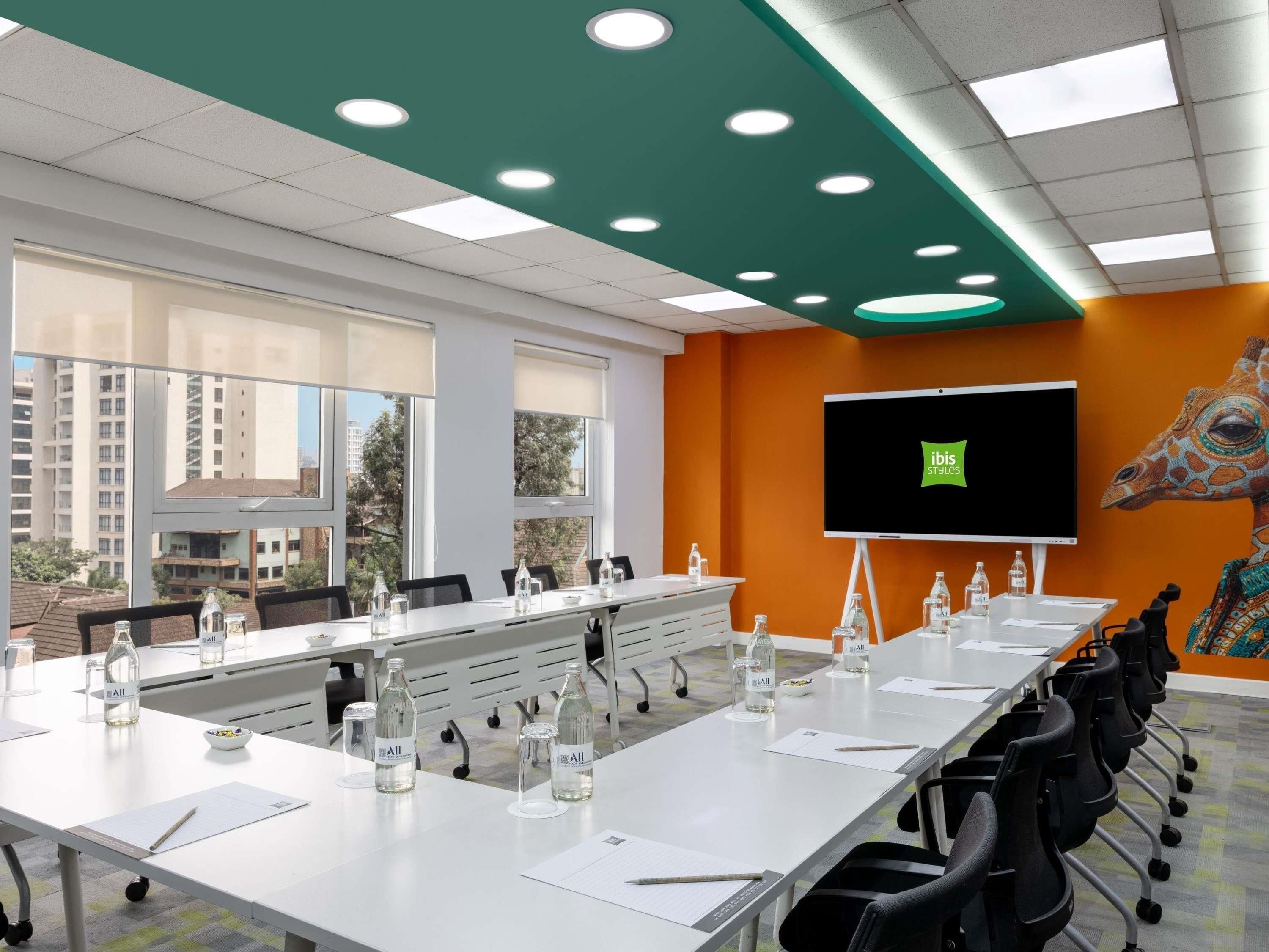 A conference room with a long table, chairs, a projector screen, and a view of buildings outside.