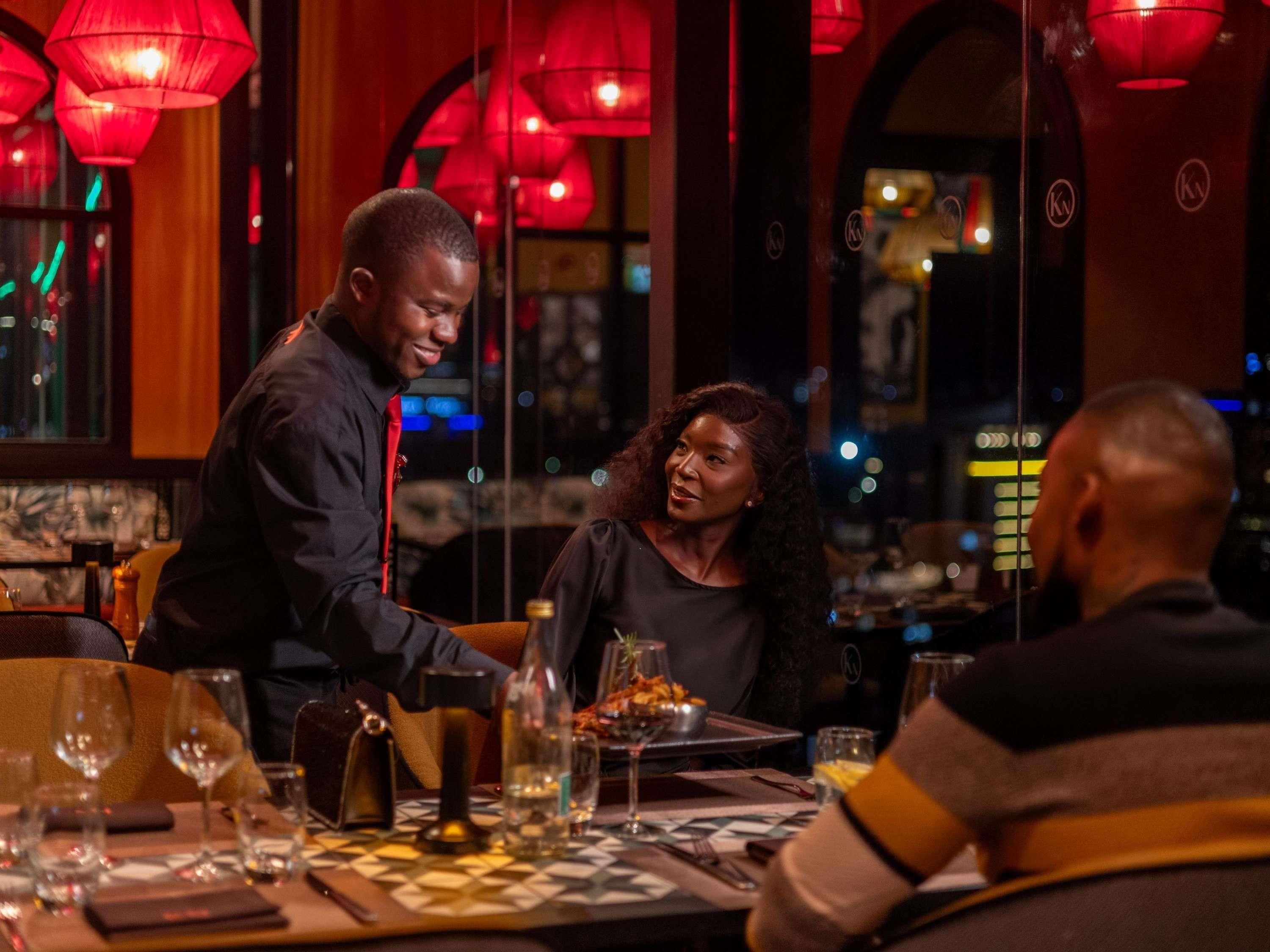 Een restaurantinterieur met tafels, stoelen en een ober die eten serveert.