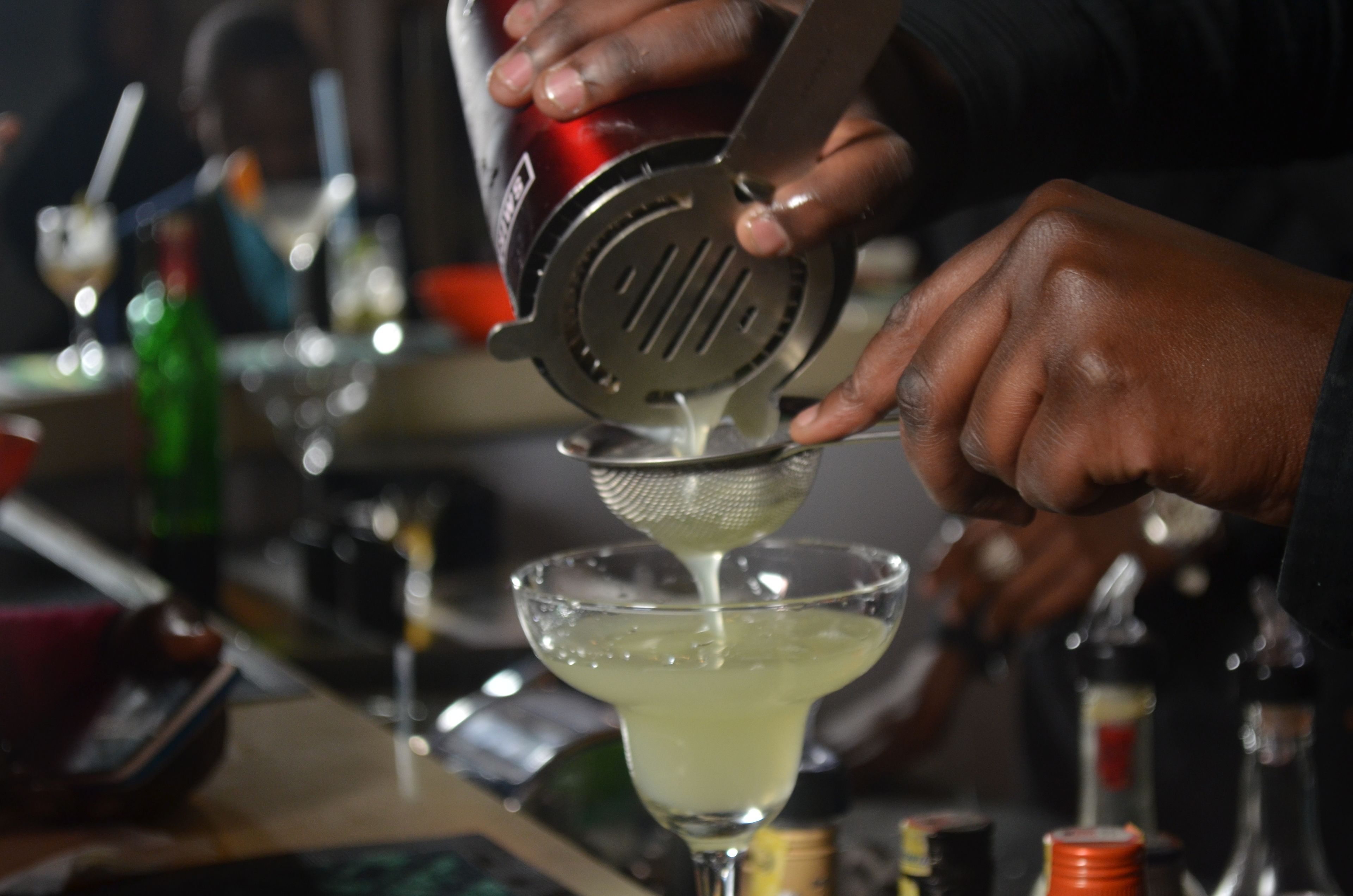 A person using a metal strainer to pour a liquid into a glass.