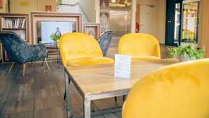 A hotel lobby with yellow chairs, a reception desk, a whiteboard, and a bookshelf. - B&B HOTEL Metz Est Technopole Pôle Santé (Peltre)