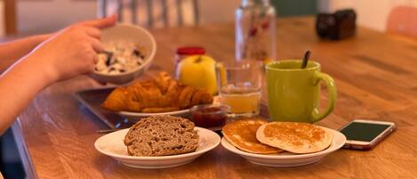 Una mesa de desayuno con cruasanes, panqueques y una taza verde.
