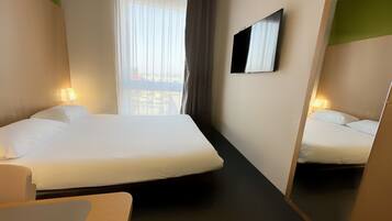 A hotel room with a bed, bedside tables, a mirror, and a window with curtains.
