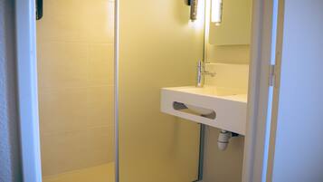 Un baño con lavamanos blanco, un espejo y cabina de ducha.