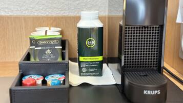 A hotel minibar setup with a bottle of B&B Hotel's water, a Krups coffee maker, and various toiletries.