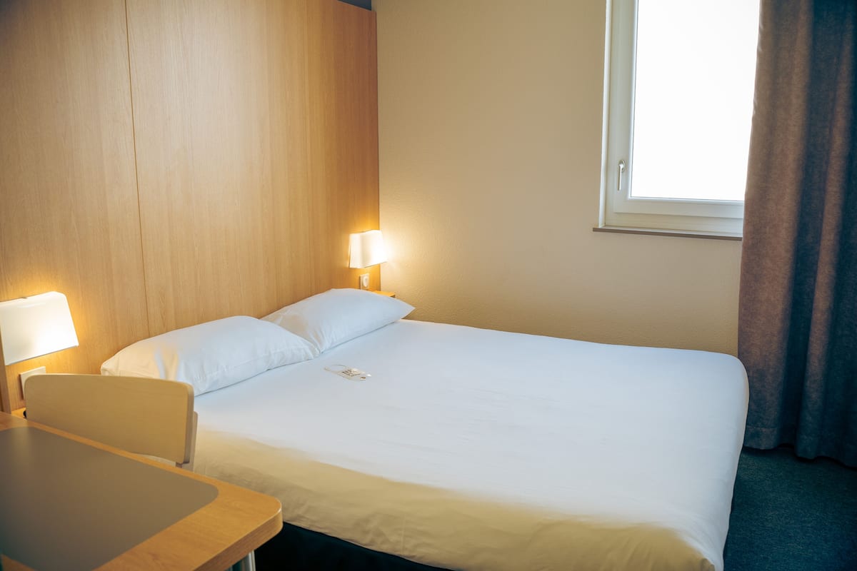 A hotel room with a bed, bedside tables, and a window with curtains.