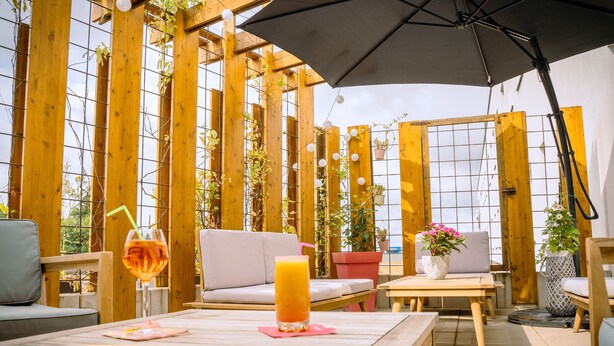 An outdoor seating area with wooden furniture, a table with drinks, and potted plants. - B&B HOTEL Metz Est Technopole Pôle Santé (Peltre)