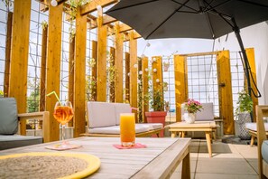 Un área de estar al aire libre con mobiliario de madera, una mesa con bebidas y plantas en macetas.