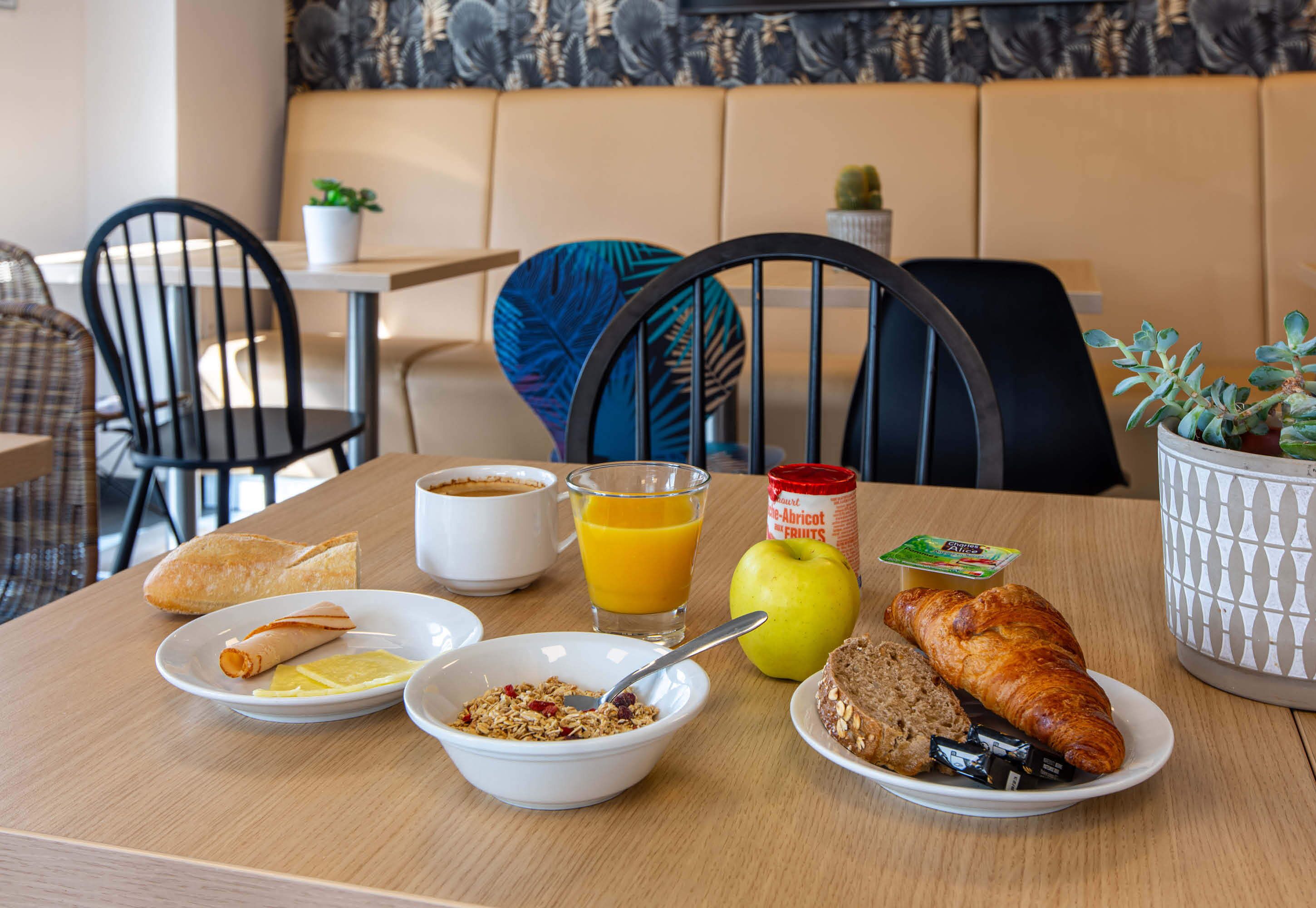 A breakfast table with croissants, a bowl of cereal, a glass of orange juice, an apple, and a croissant on a plate.