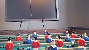 Una mesa de fútbol de mesa con dos equipos, una pizarra con 'Equipe 1' y 'Equipe 2' escritas, y una pared con 'BABY FOOT' escrito en letras grandes.