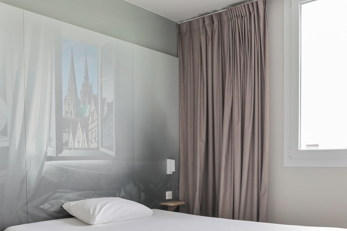 A modern bedroom with a large bed, a nightstand, a window with curtains, and a mural on the wall.