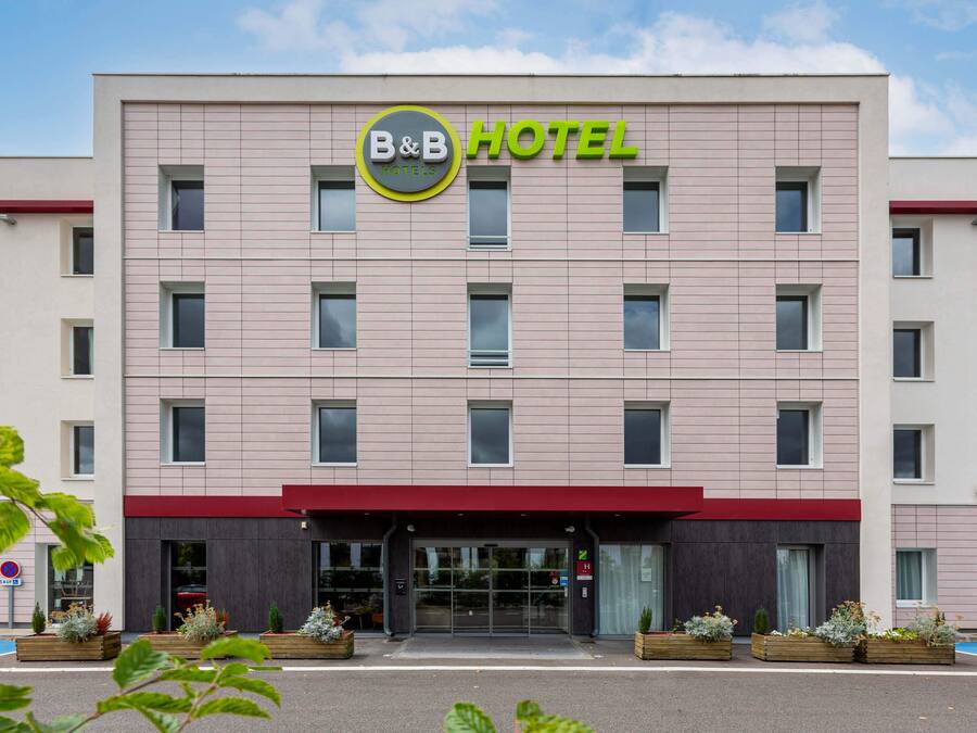 Un hôtel-restaurant de type « bed and breakfast » doté d’une façade moderne, de nombreuses fenêtres et d’un auvent rouge.