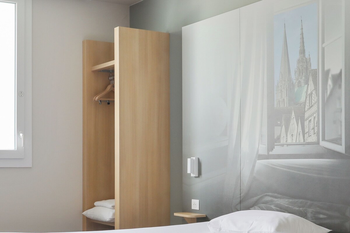 A modern bedroom with a large bed, a wooden wardrobe, a nightstand, and a wall-mounted light.