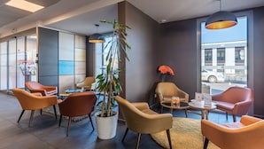 A modern lobby with leather chairs, a potted plant, and a view of the street.