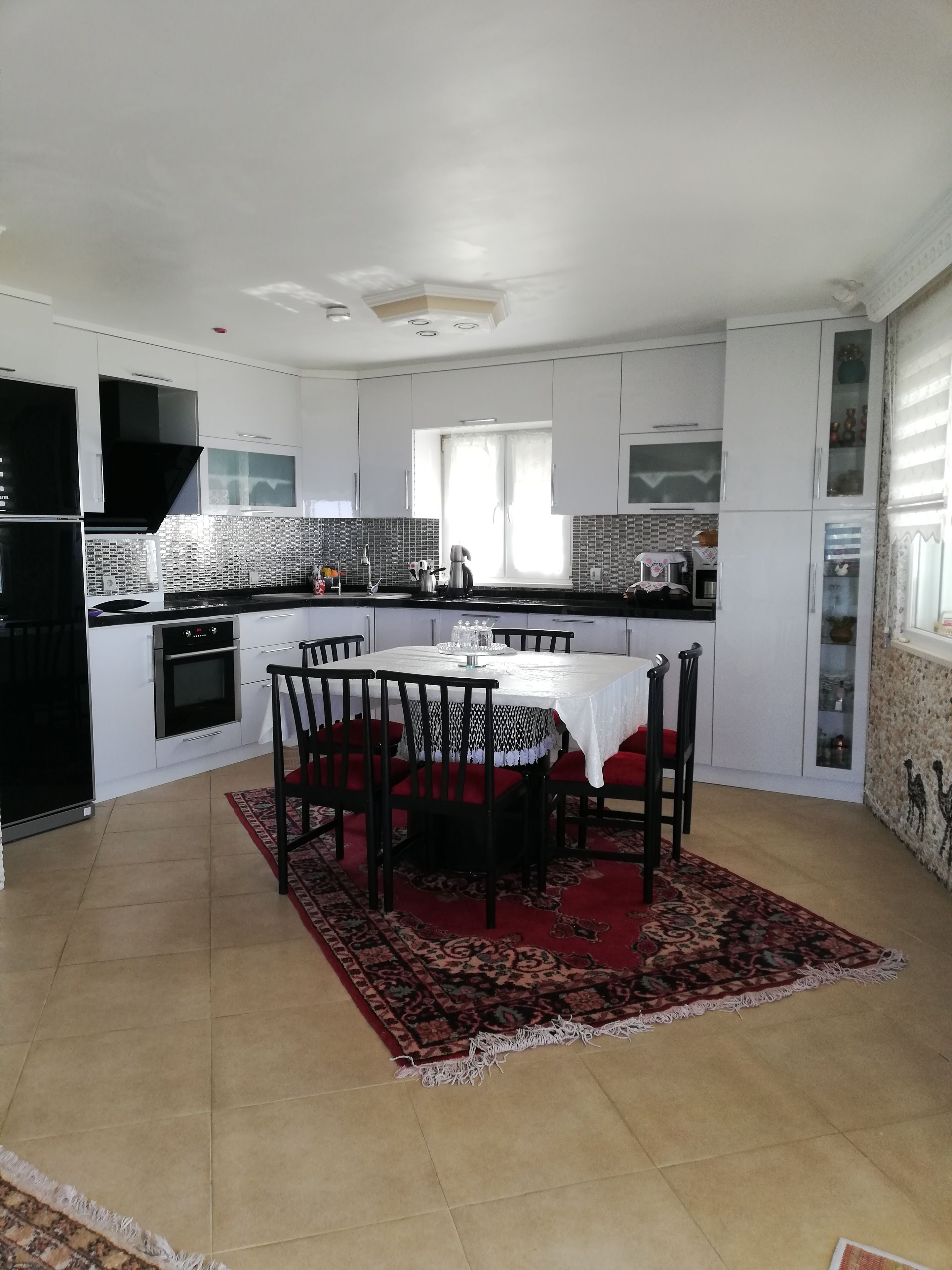 Une cuisine moderne avec des meubles blancs, une hotte noire et un coin repas comprenant une table et des chaises.