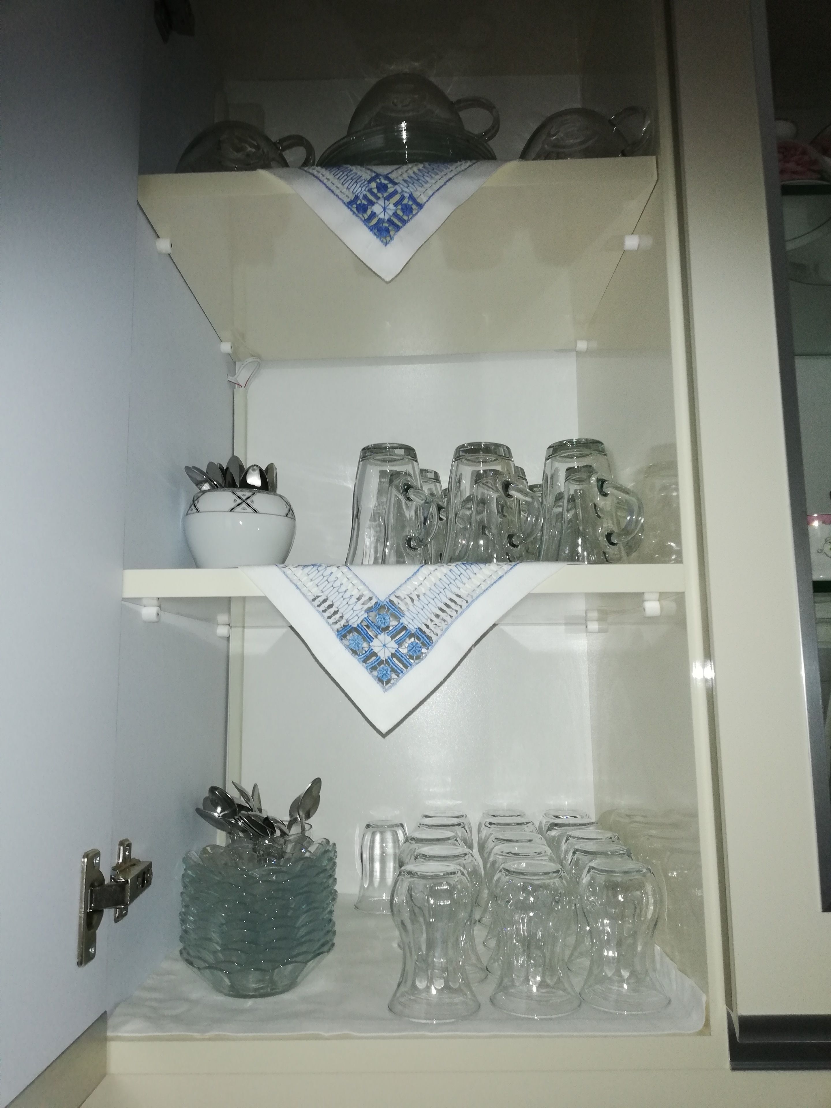 Ein Küchenschrank mit Regalen, die Gläser, eine Schale und einen dekorativen Glasbehälter enthalten.