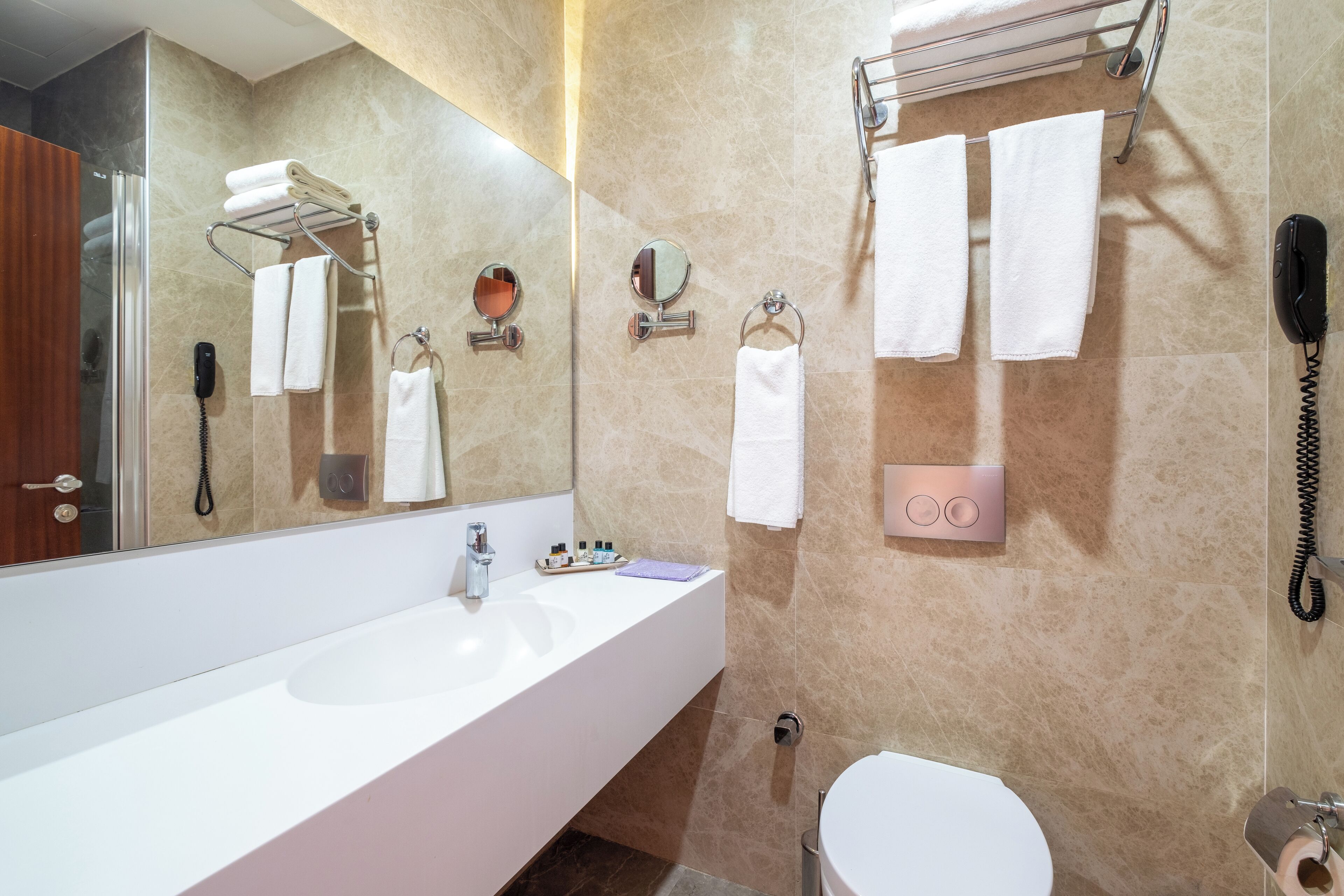 A modern bathroom with a large mirror, a white sink, a toilet, and a shower area.