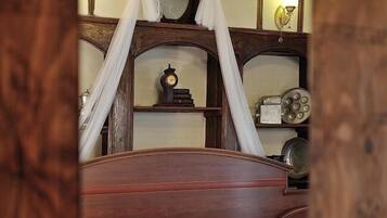 Une chambre à coucher avec un lit à baldaquin, une table de chevet, un miroir et une étagère ornée d’objets décoratifs.