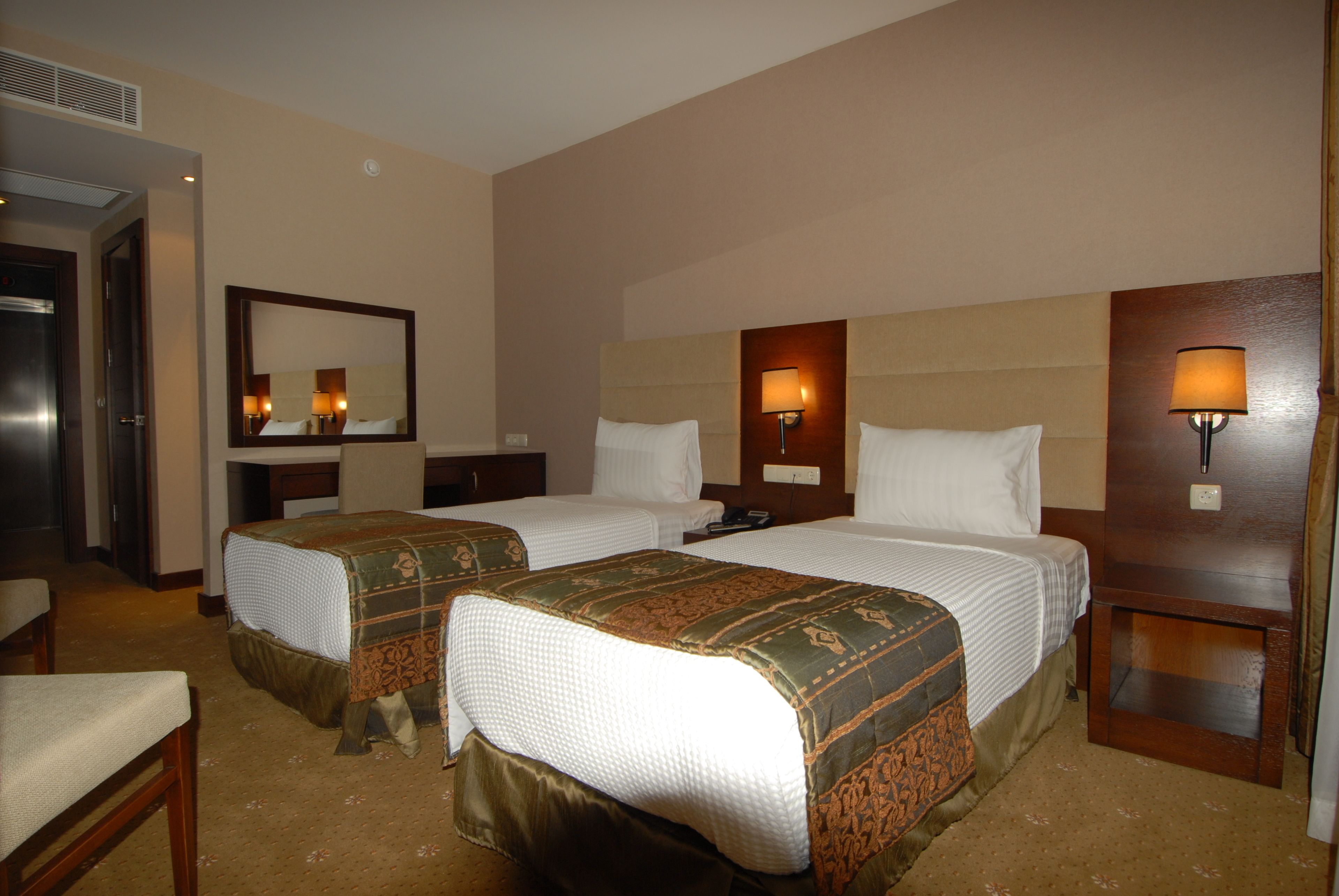 A hotel room with two beds, a mirror, bedside lamps, and a chair.