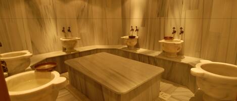 A modern bathroom with a large central bathtub, two sinks, and three toilets.
