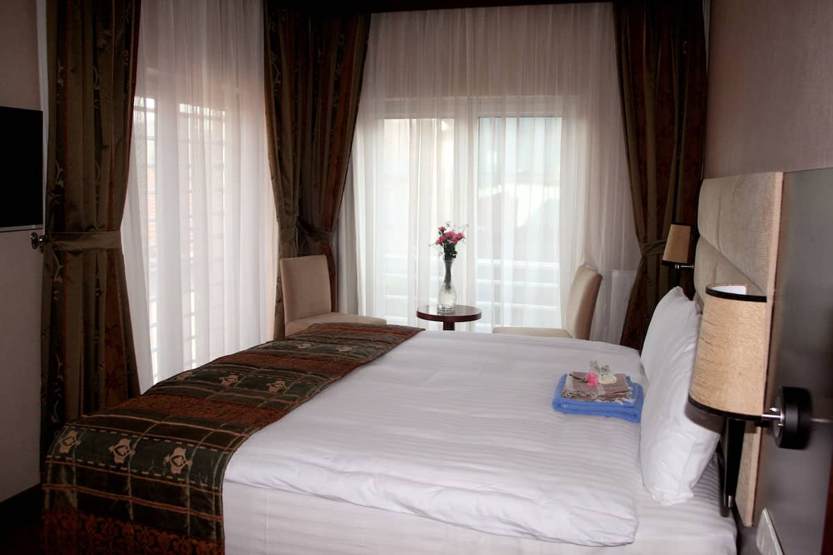 Habitación de hotel con una cama grande, una mesita con un florero y una lámpara en la mesita de noche.