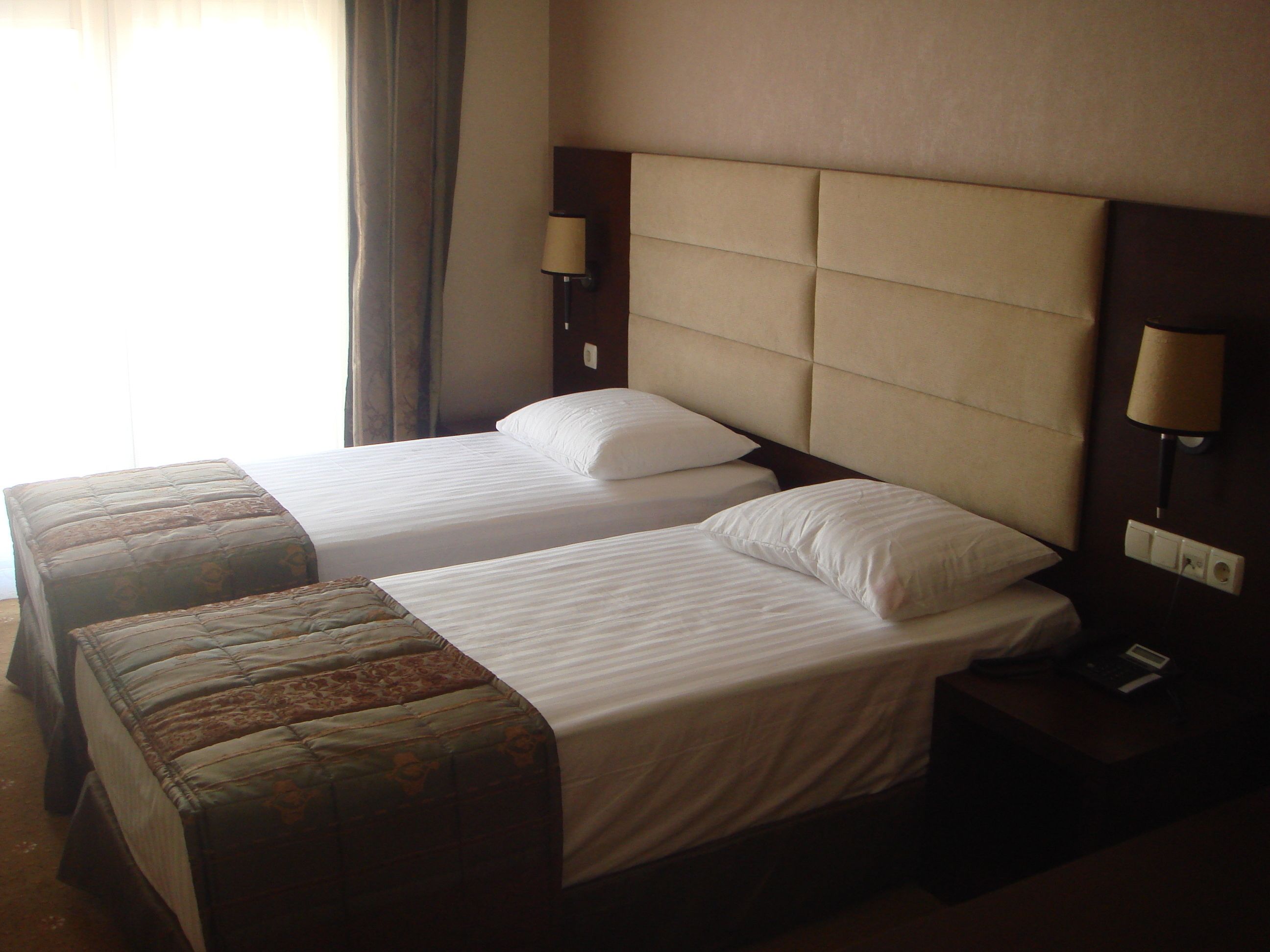 Een hotelkamer met twee bedden, een nachtkastje met een lamp en een raam met gordijnen.