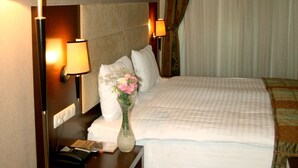 A hotel room with a bed, two bedside lamps, a nightstand with a telephone, and a vase with flowers. - Cetin Otel (Kesan)