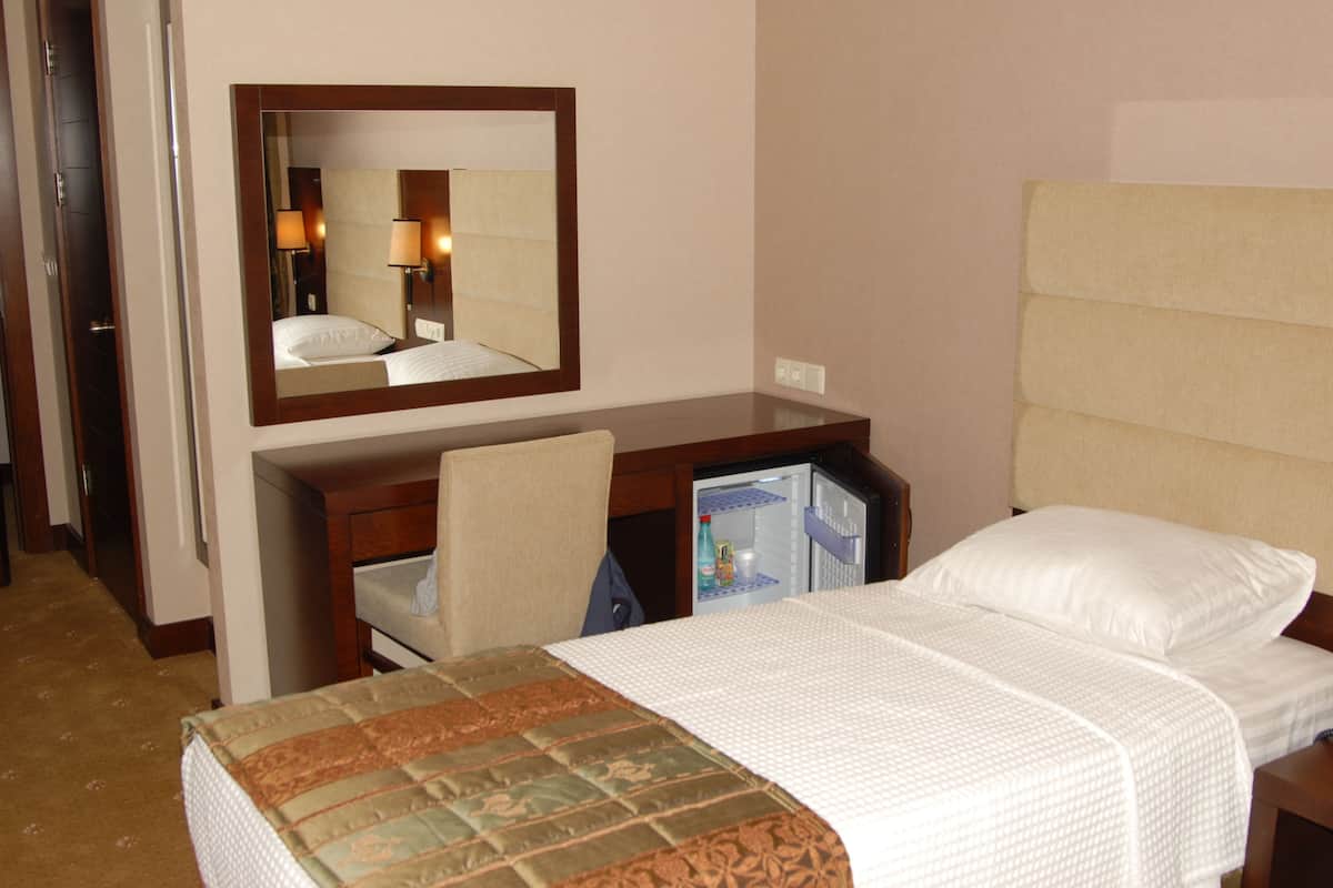 Una habitación de hotel con una cama, un escritorio, una silla, un espejo y un mini bar.