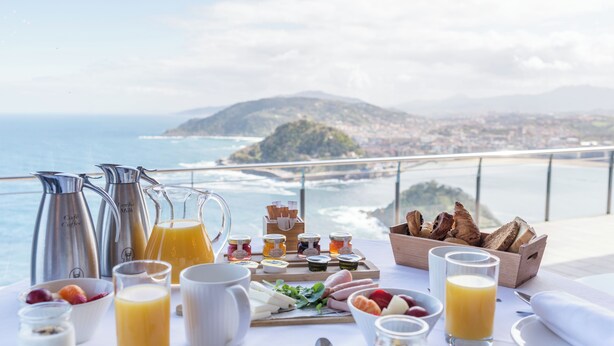 A breakfast table with various food items and drinks, overlooking a scenic coastal view. - Mercure San Sebastian Monte Igueldo (San Sebastián)