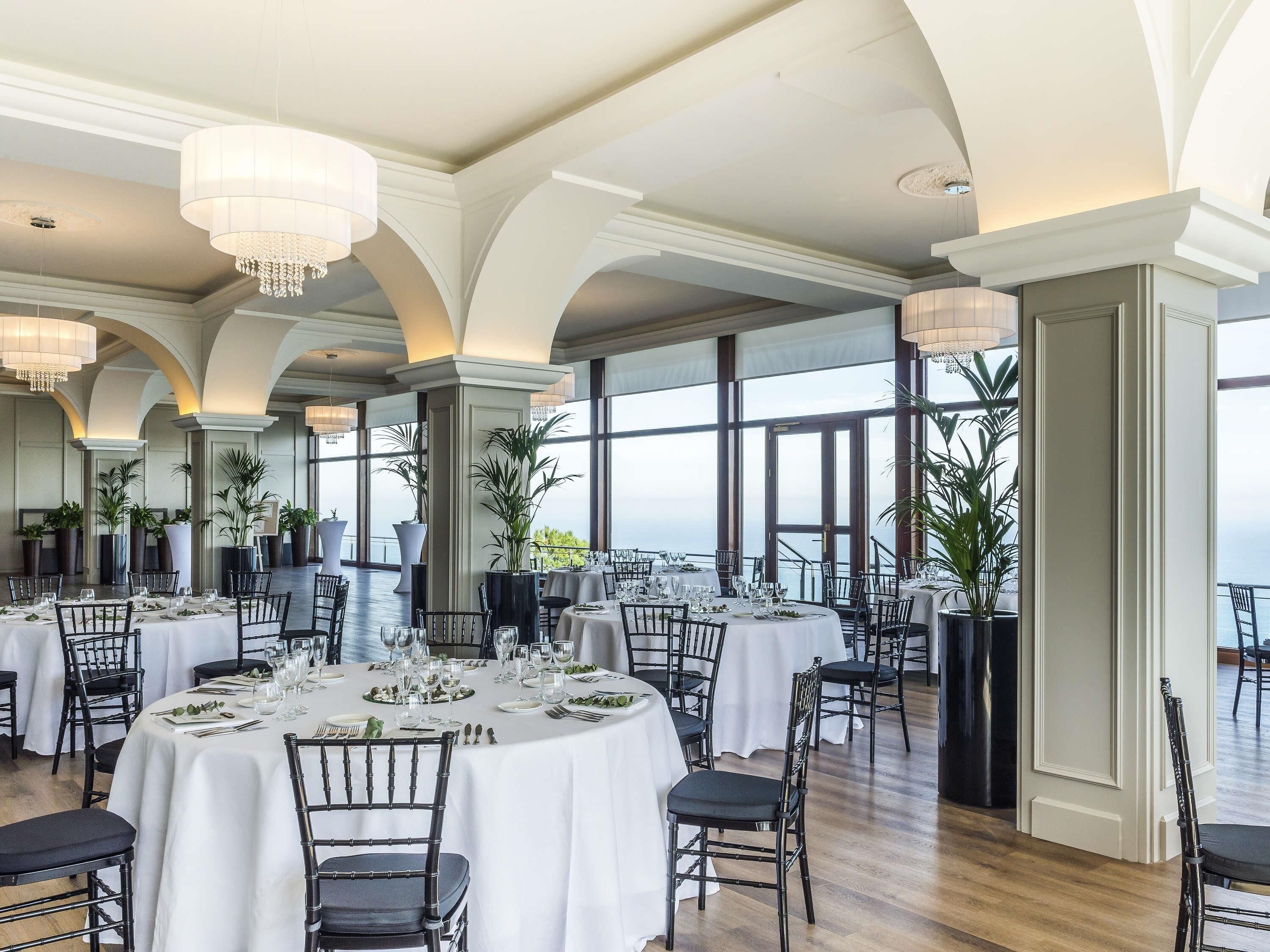 A spacious dining area with round tables, black chairs, and large windows offering a view.