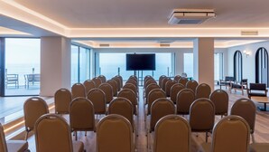 A conference room with rows of chairs facing a large screen, large windows, and a view of the sea. - Mercure San Sebastian Monte Igueldo (San Sebastián)