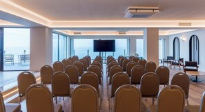 A conference room with rows of chairs facing a large screen, large windows, and a view of the sea. - Mercure San Sebastian Monte Igueldo (San Sebastián)