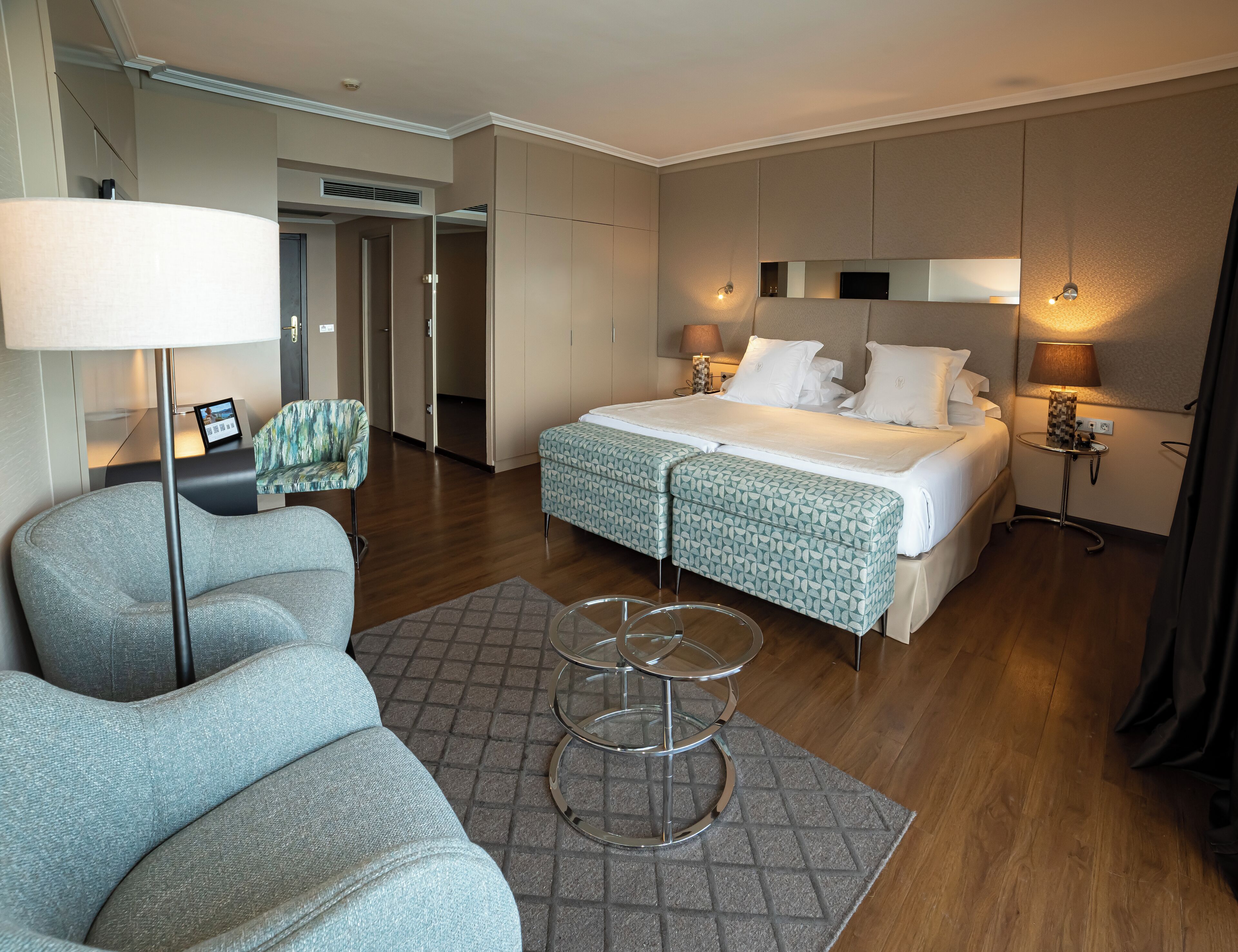 A hotel room with a bed, a chair, a small table, and a lamp.