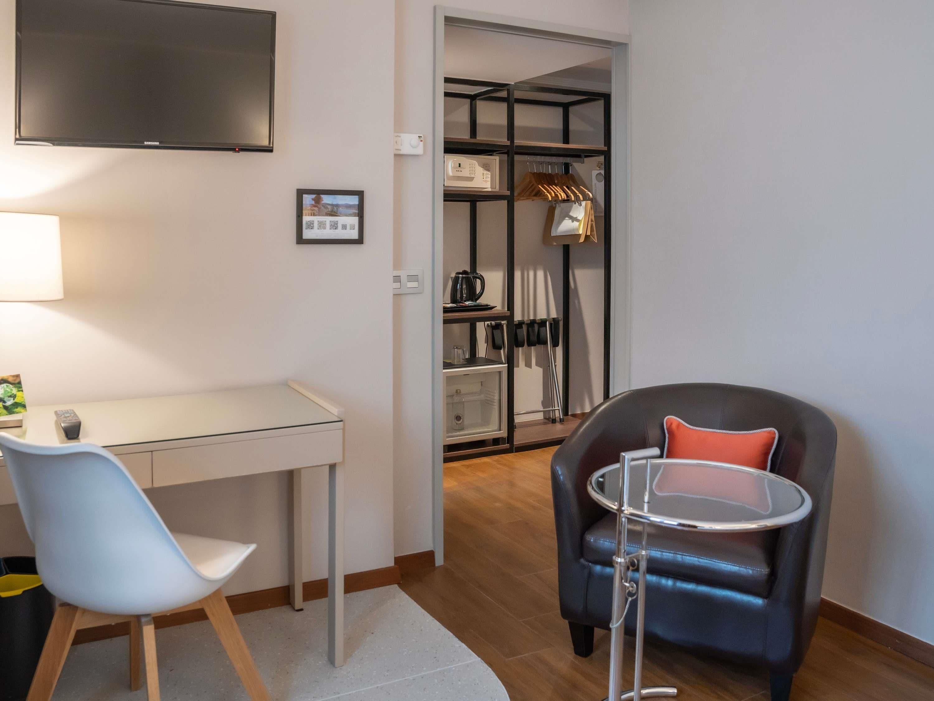Una habitación moderna con escritorio, una silla, una mesa redonda y un armario con estantes y espacio para colgar.