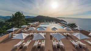 A poolside area with sun loungers and umbrellas, overlooking a body of water and hills. - Mercure San Sebastian Monte Igueldo (San Sebastián)
