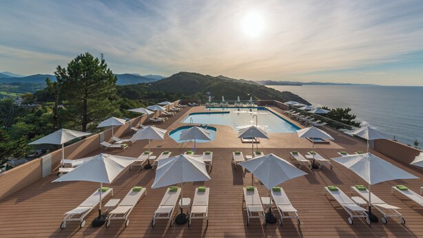 A poolside area with sun loungers and umbrellas, overlooking a body of water and hills. - Mercure San Sebastian Monte Igueldo (San Sebastián)