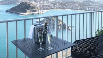 Een balkon met een tafel waarop een champagnefles en twee glazen staan, met uitzicht op een kustplaats.