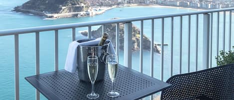 A balcony with a table holding a champagne bottle and two glasses, overlooking a coastal cityscape.