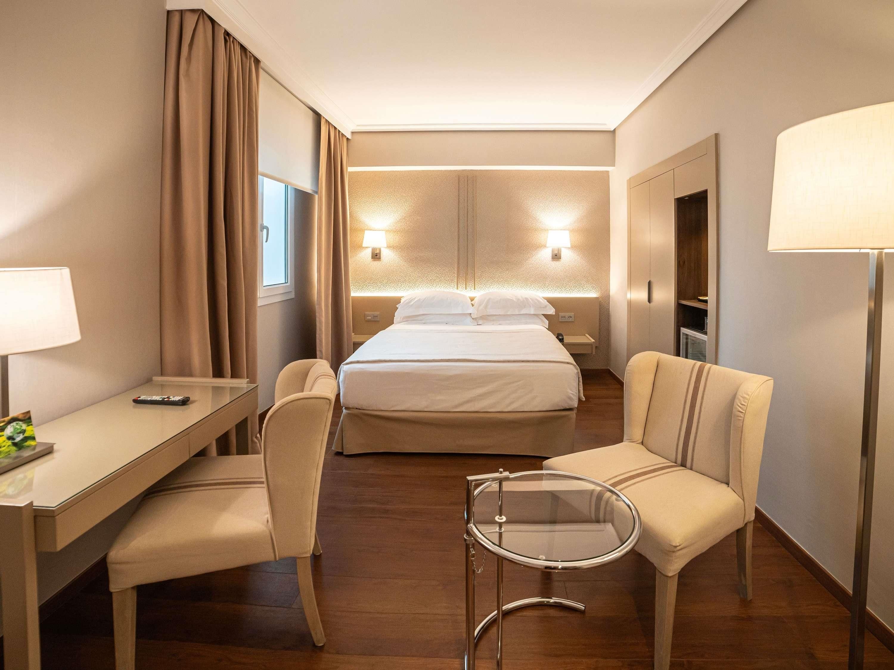 Et hotelværelse med seng, skrivebord, stol, lille bord og lampe.
