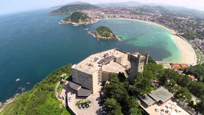 An aerial view of a coastal town with a prominent castle-like structure, a beach, and a marina. - Mercure San Sebastian Monte Igueldo (San Sebastián)