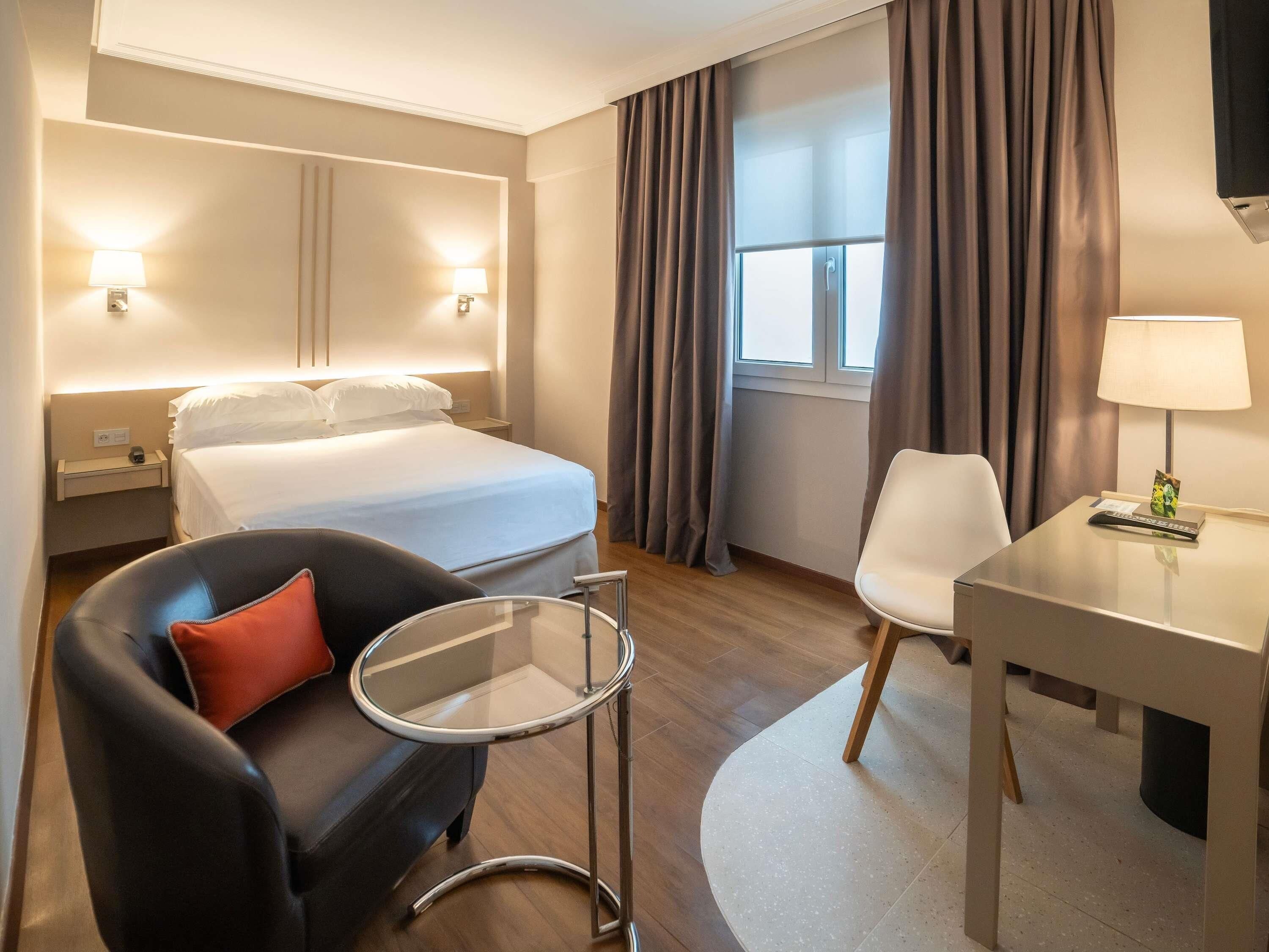 Una habitación de hotel con cama, escritorio, silla, mesita y lámpara.