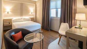 Una habitación de hotel con cama, escritorio, silla, mesita y lámpara.