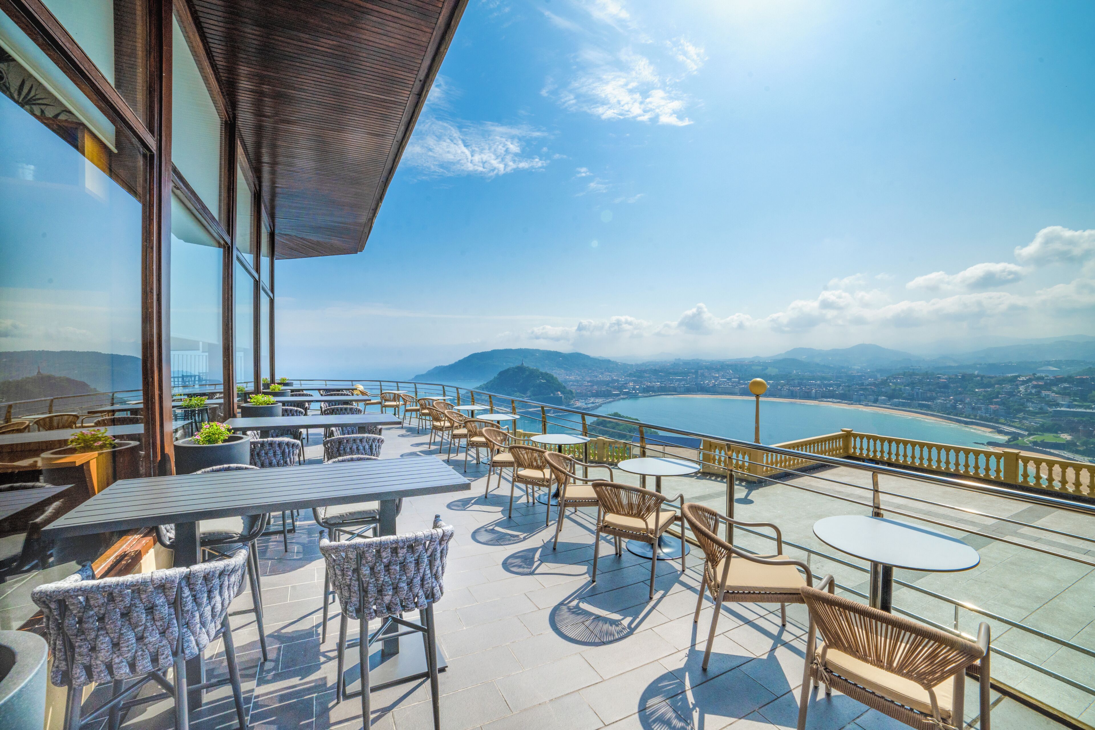 Una terraza con asientos al aire libre, vista al mar y montañas a lo lejos.