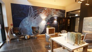 A modern lobby with a large abstract mural, comfortable seating, a reception desk, and a decorative plant centerpiece. - Easy Living Hotel (List)