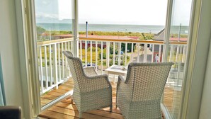 A balcony with wicker chairs and a table, overlooking a beach and buildings. - Easy Living Hotel (List)